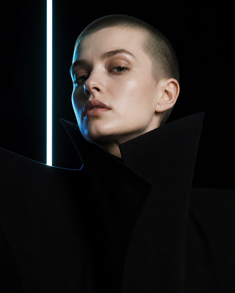 Synthetic close portrait with cropped hair, black sculptural clothing, and cyan edge light